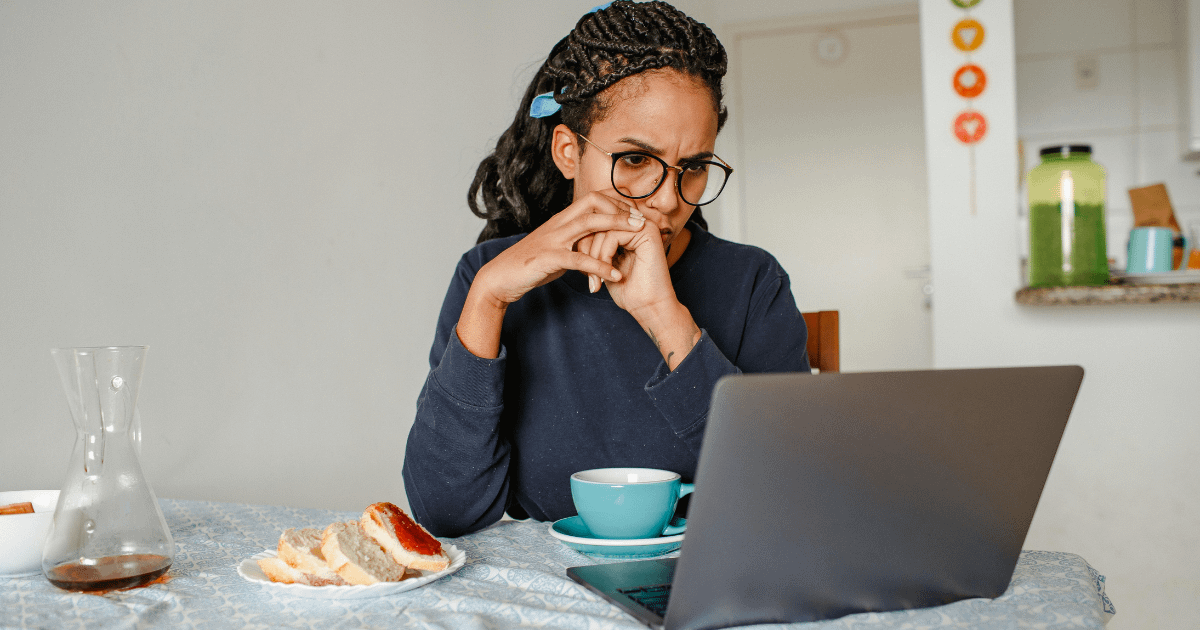A woman sits at her kitchen table, laptop open, looking intently at the screen - capturing the exhausting reality of searching for a child's therapist while navigating insurance.