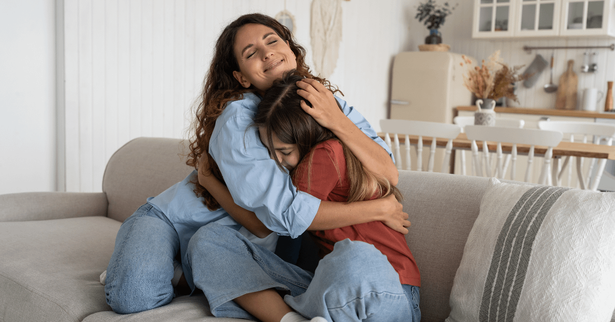 Mother and young teen daughter hugging on the couch.