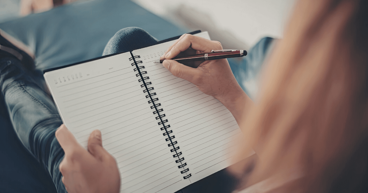 A parent taking notes in a spiral notebook while preparing questions to ask a child therapist.